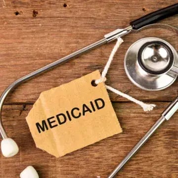 A stethoscope on a wood surface with a tag that says Medicaid next to it