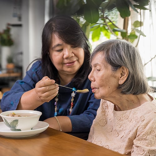 A woman feeding soup to her elderly mother